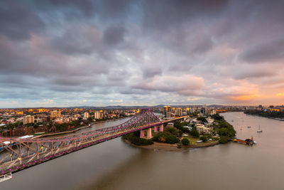 Bridge over river in city against cloudy sky