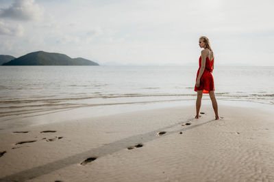 Rear view of woman walking at beach against sky