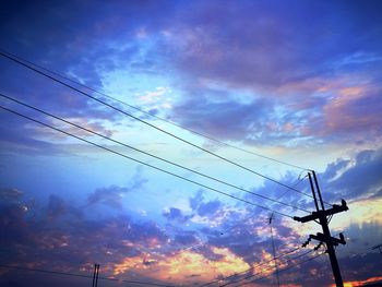 Low angle view of silhouette electricity pylon against dramatic sky