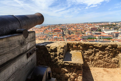 Close-up of old cannon by retaining wall in city against sky