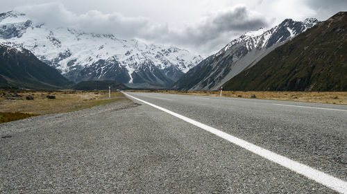 Road leading towards snowcapped mountains against sky