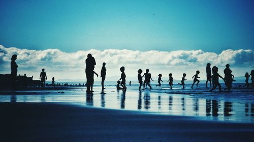 Silhouette people at beach against sky