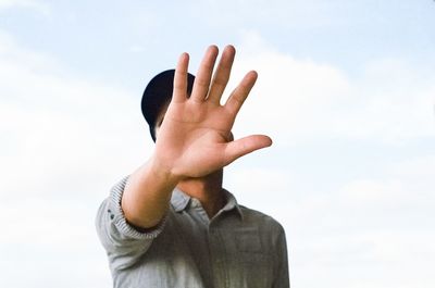 Close-up of man showing stop gesture while standing against sky