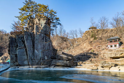 Rock formation by lake against clear sky