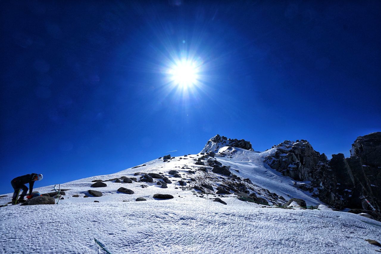 snow, mountain, leisure activity, cold temperature, sky, beauty in nature, real people, winter, scenics - nature, snowcapped mountain, one person, sunbeam, lifestyles, nature, adventure, unrecognizable person, tranquility, mountain range, non-urban scene, sun, lens flare, outdoors, bright