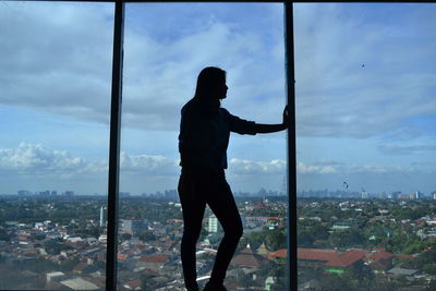 Man standing by window in city against sky