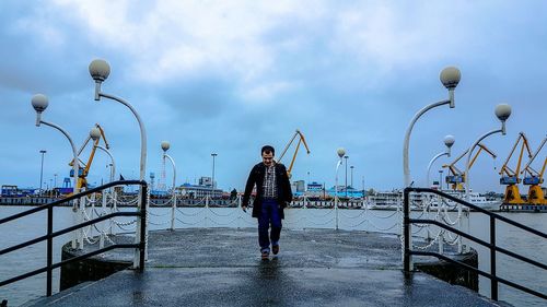 Man walking on promenade by sea against cloudy sky