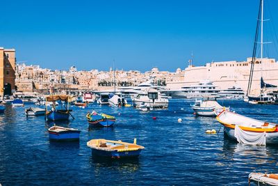 Boats moored at harbor against clear blue sky