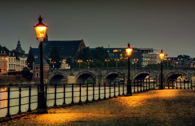 Illuminated street light by river against sky in city at night