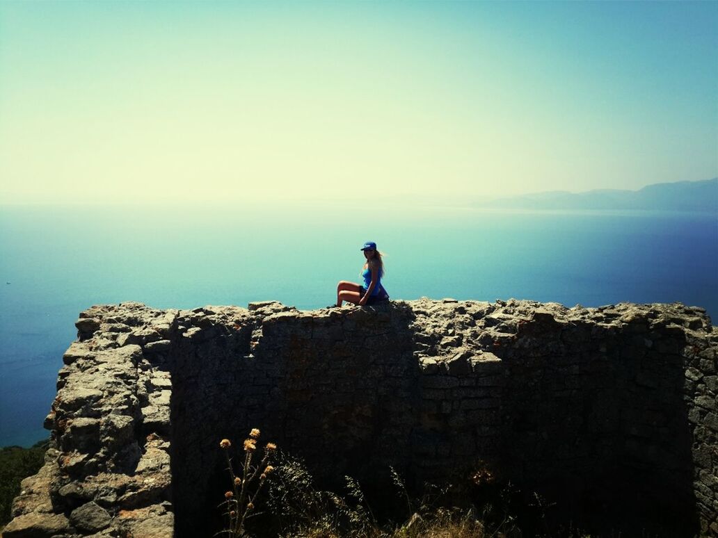 sea, horizon over water, lifestyles, copy space, leisure activity, clear sky, silhouette, water, rock - object, standing, sky, full length, tranquility, tranquil scene, nature, men, scenics, rock