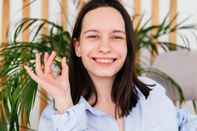 Smiling young woman with short hair holding pill omega capsule in hand at home. girl taking medicine