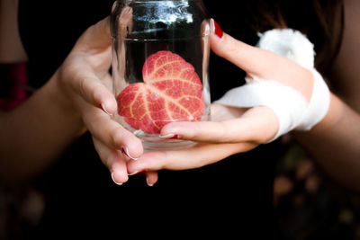 Close-up of injured hand holding leaf in glass