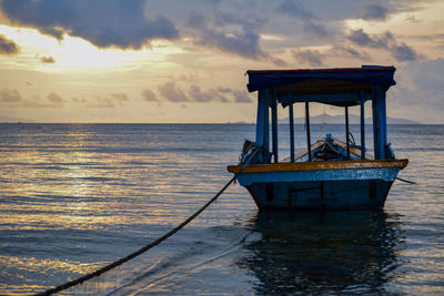 Stilt house on sea against sky during sunset