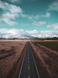 Empty road along countryside landscape towards snow capped mountains