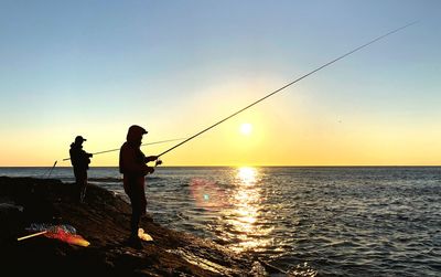 Silhouette man fishing at sea against sky during sunset