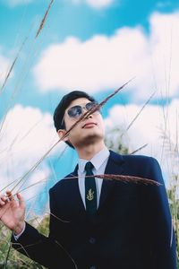 Portrait of young man holding camera against sky