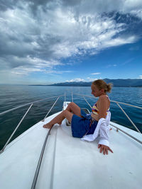 Boy sitting on boat in sea against sky