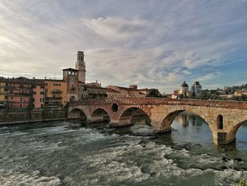 Arch bridge over river by buildings against sky