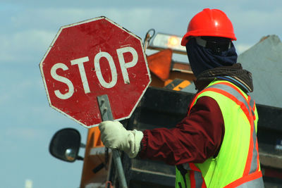 Side view of male worker holding stop sign against vehicle on road