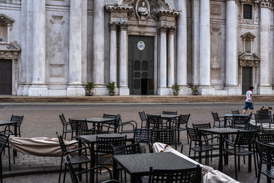 A boy walking with his dog and empty tables and chairs in front of the new cathedral in brescia. 