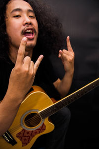 Portrait musician with guitar showing horn sign against black background