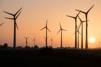 Silhouette wind turbines on field against sky during sunset