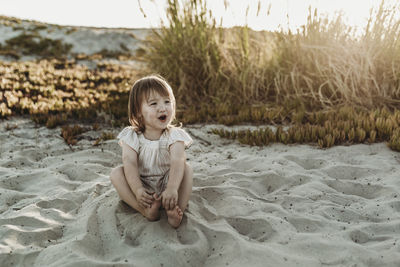 Front view of young toddler girl looking away and laughing at beach