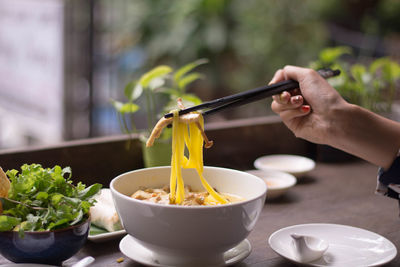 Cropped image of hand holding bowl of table