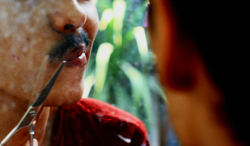 Close-up of man cutting mustache with scissors