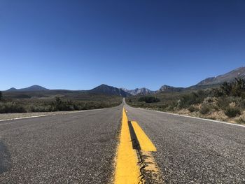 Surface level of road by mountains against clear blue sky