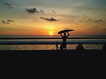 Silhouette people on beach against sky during sunset