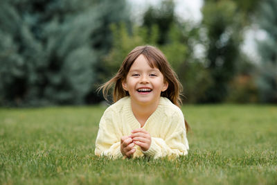 Funny smiling blonde little child girl 4-5 year old lying on green grass lawn outdoor. 