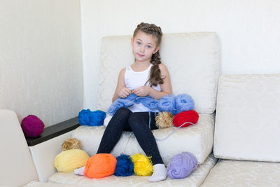 Portrait of smiling girl with wool sitting on sofa at home