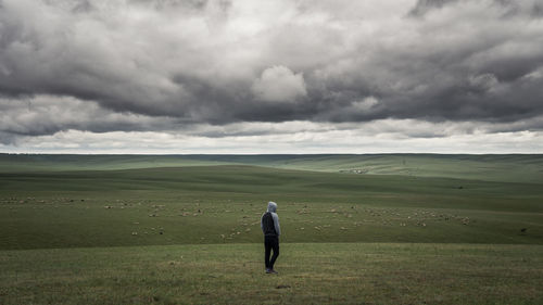 Rear view of man standing on grassy field against cloudy sky