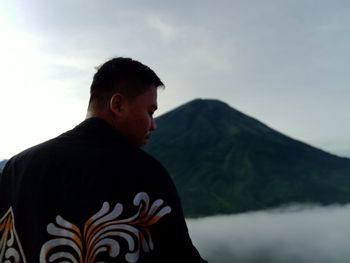 Rear view of man looking at mountains against sky