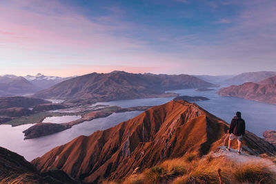 Man looking at mountain range against sky during sunset