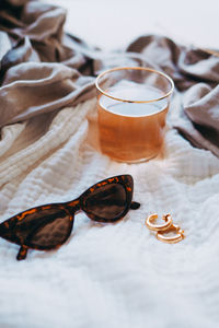 High angle view of earrings and sunglasses with drink on bed