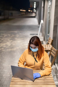 High angle view of businesswoman wearing mask using laptop in cafe at night