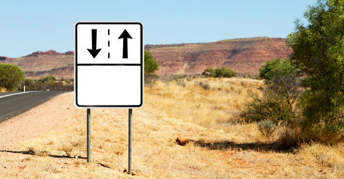 Information sign on road amidst field against clear sky