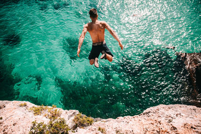 Full length of shirtless man jumping in sea