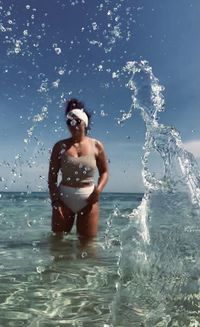 Full length of shirtless man splashing water in sea