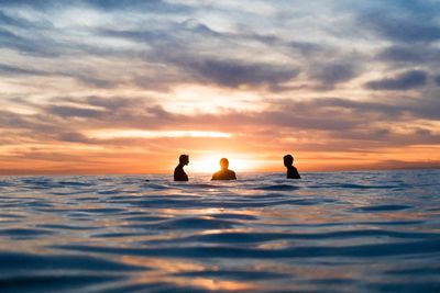 Silhouette men in sea against sky during sunset