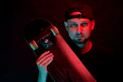 Portrait of man holding skateboard against black background