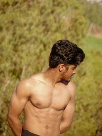 Shirtless young man looking away while standing on land