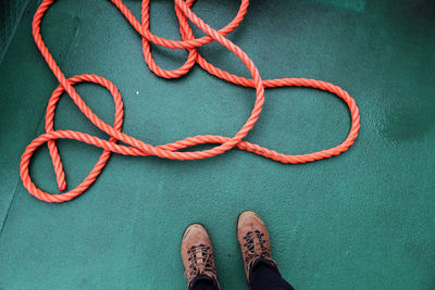 Low section of man standing by rope on boat deck