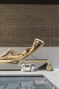 Vertical view of young woman with eyes closed sun bathing getting tan laying on a lounger in summer