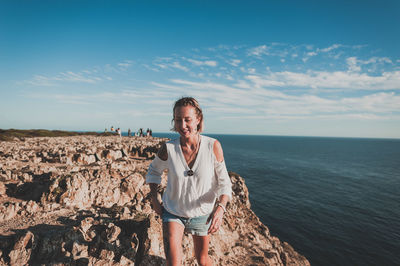 Portrait of smiling woman standing on rock against sea