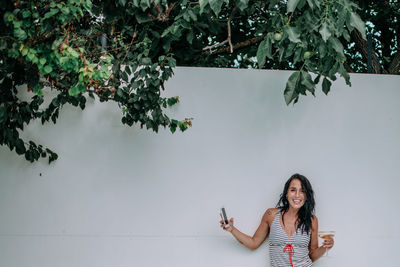 Portrait of smiling young woman standing against wall