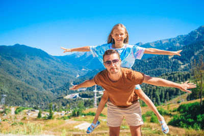 Full length of happy man with arms outstretched against mountain against sky