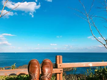 Low section of man wearing brown shoes at beach against sea and sky